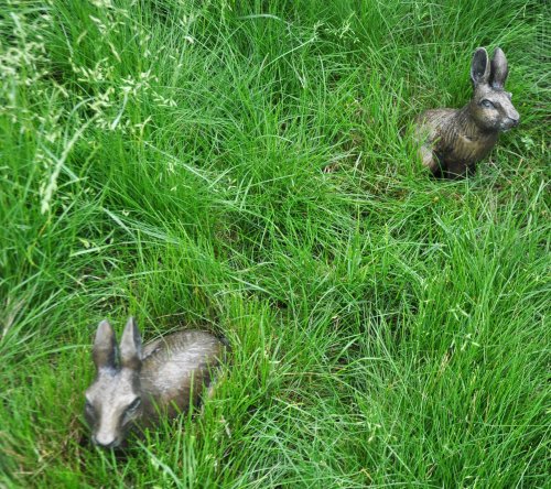 Two bronze rabbit sculptures nestled in lush green grass.
