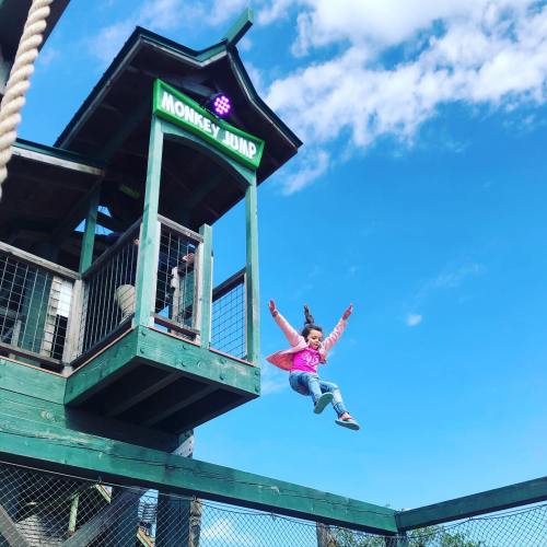 A child in a pink vest jumps from a platform labeled "Monkey Jump" against a blue sky.