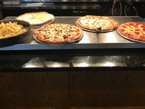 A buffet display featuring various pizzas and a tray of macaroni and cheese on a countertop.