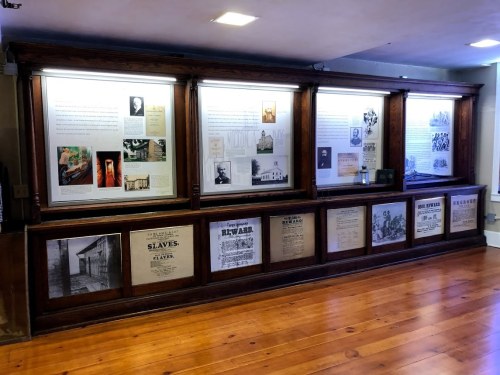 A wooden display case with historical documents and images, showcasing information about slavery and its impact.