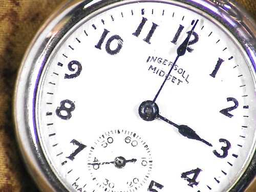 Close-up of a vintage Ingersoll pocket watch, featuring a white face with black numbers and a small subdial.