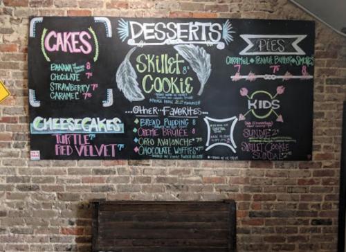 Chalkboard menu featuring desserts: cakes, cheesecakes, pies, and kids' options with prices listed.