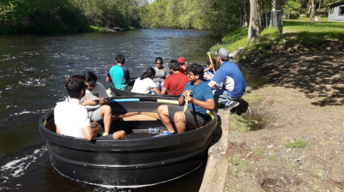 A group of people sitting in a circular boat on a river, enjoying a sunny day surrounded by greenery.