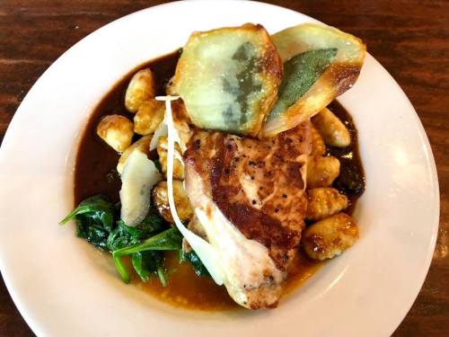 A plate of gnocchi topped with grilled fish, sautéed spinach, and crispy greens in a savory sauce.