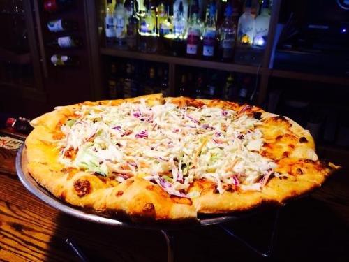 A large pizza topped with shredded cabbage, sitting on a metal stand in a bar setting with bottles in the background.