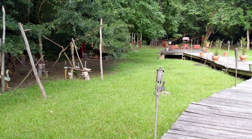 A wooden pathway leads to a grassy area with rustic structures and trees in the background.