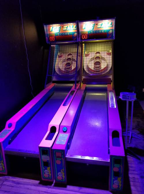 Two illuminated skee-ball machines in a dark room, featuring colorful designs and score displays.
