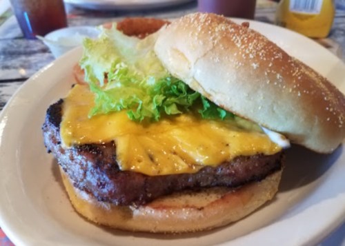 A close-up of a cheeseburger with lettuce and a slice of pineapple on a sesame seed bun, served on a plate.