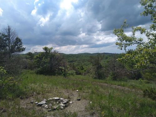 A scenic view of rolling green hills under a cloudy sky, with a stone circle in the foreground.