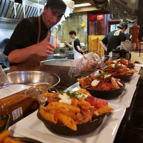 A chef gives a thumbs up in a busy kitchen, showcasing dishes in cast iron skillets on the counter.