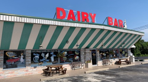A retro-style dairy bar with a striped awning, large "DAIRY BAR" sign, and outdoor seating.