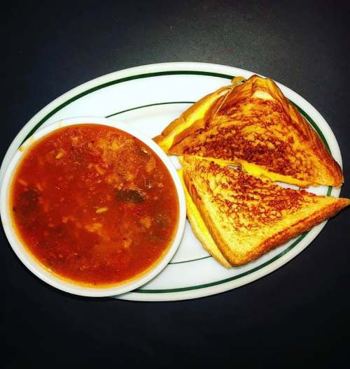 A plate with a bowl of tomato soup and a grilled cheese sandwich, golden brown and cut in half.