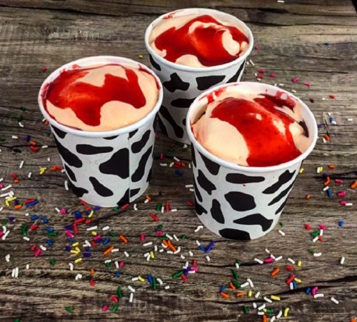 Three cups of ice cream with red syrup on top, placed on a wooden surface sprinkled with colorful confetti.