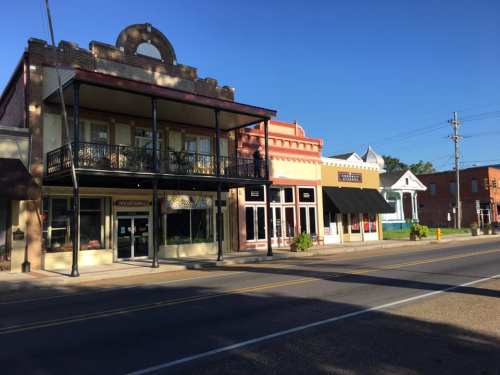 A row of charming storefronts with balconies and colorful facades along a quiet street under a clear blue sky.