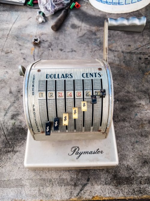 A vintage Paymaster cash register with dials for dollars and cents, resting on a workbench.