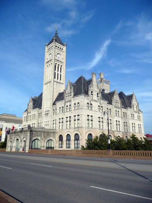 Historic stone building with a tall clock tower, featuring intricate architectural details against a blue sky.