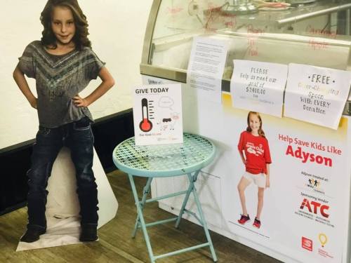 A life-size cutout of a girl stands next to a donation thermometer and a poster promoting help for kids like Adyson.