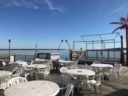 Outdoor seating area by the water with white tables and chairs, a dock, and a clear blue sky.