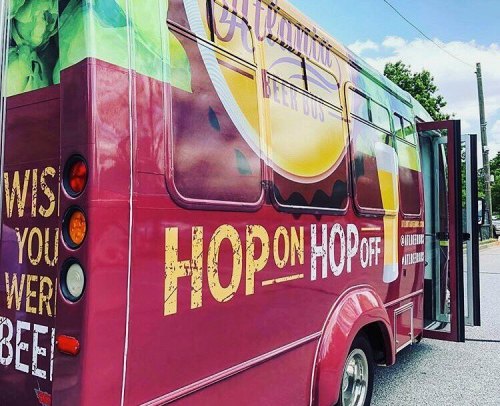 A colorful beer bus with the text "Hop On Hop Off" and a beer-themed design parked on a street.