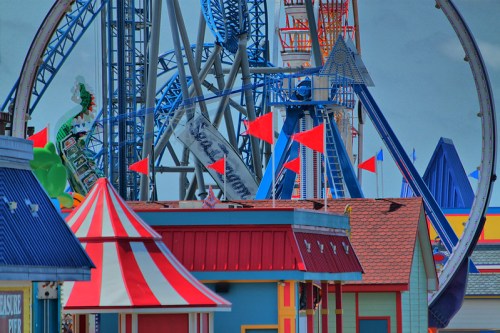 Colorful amusement park scene featuring roller coasters, flags, and vibrant carnival-style buildings.