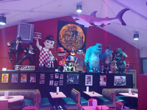 Colorful restaurant interior featuring various character statues and artwork on the walls, with checkered tablecloths.