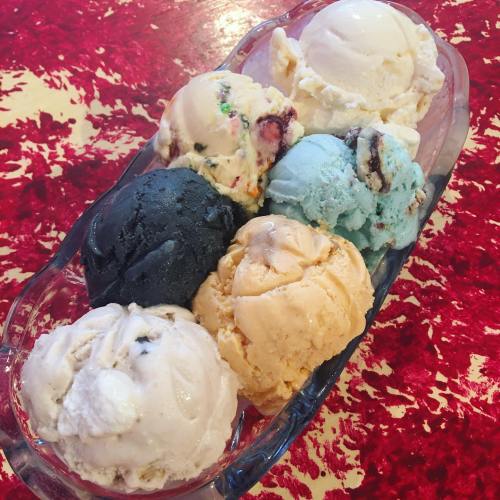 A glass dish filled with seven colorful scoops of ice cream, including black, blue, orange, and white flavors.
