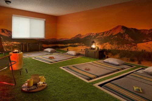 A cozy room with grass-like flooring, sleeping mats, and a mountain mural, creating a serene, nature-inspired atmosphere.
