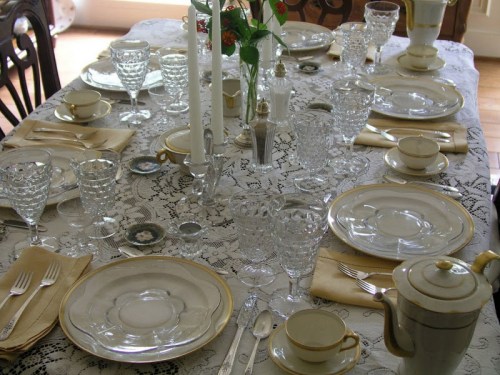 A beautifully set dining table with elegant glassware, fine china, and a lace tablecloth, ready for a meal.