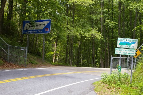 A road sign welcomes visitors to Tennessee, with a highway adoption sign nearby, surrounded by lush green trees.