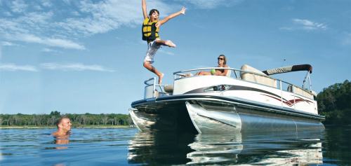 A child in a life jacket jumps off a boat into the water, while two adults relax on the boat.