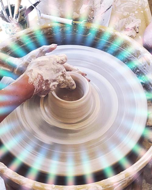 A close-up of hands shaping clay on a pottery wheel, with a colorful light effect surrounding the scene.
