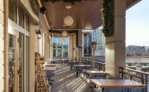Outdoor dining area of Tupelo Honey restaurant, featuring wooden tables, blue chairs, and decorative hanging lights.