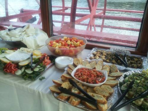 A variety of colorful dishes including fruit, vegetables, and dips arranged on a table by a window overlooking water.