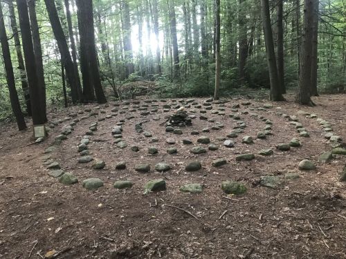A stone labyrinth in a forest, surrounded by trees, with a central pile of stones and a serene, natural atmosphere.