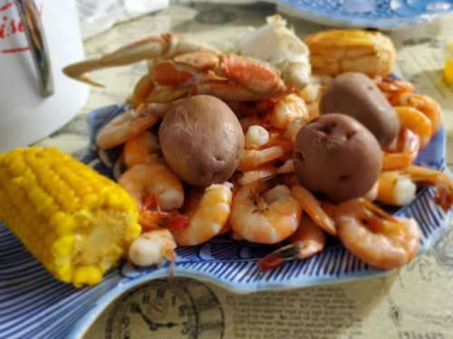 A blue plate filled with shrimp, crab, potatoes, and corn on a textured table surface.