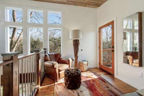 Cozy corner with a leather chair, a round ottoman, and large windows letting in natural light.