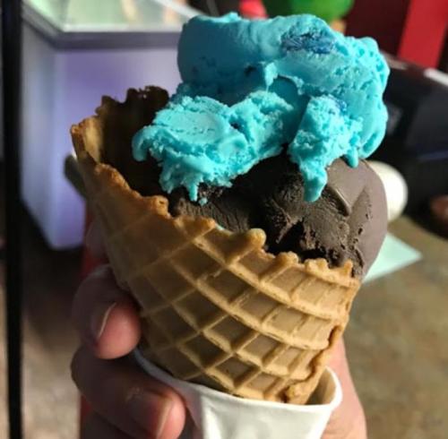 A hand holding a waffle cone filled with chocolate and blue ice cream.