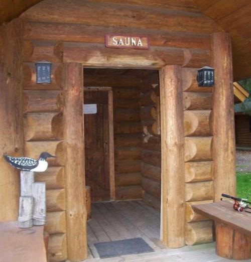 Entrance to a rustic wooden sauna with a sign above the door and a decorative bird nearby.