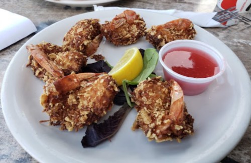 A plate of crispy fried shrimp with a lemon wedge and a small cup of dipping sauce.