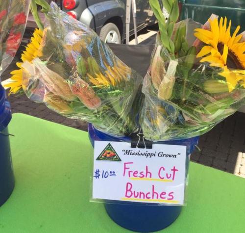 A bucket of fresh cut flower bunches, including sunflowers, with a sign displaying the price of $10.