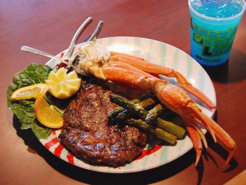 A plate featuring a steak, crab legs, asparagus, lemon slices, and a blue drink.