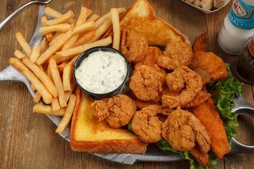 A platter of fried shrimp, fish fillets, toast, and French fries, served with a side of tartar sauce.