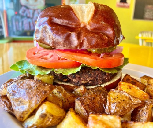 A close-up of a veggie burger with lettuce, tomato, and pickles, served with crispy roasted potatoes on the side.