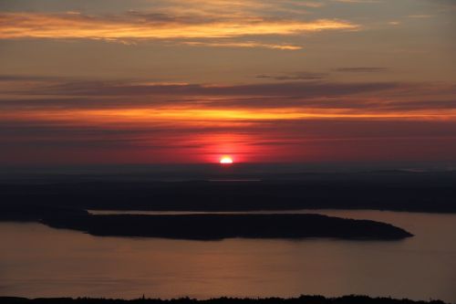 A vibrant sunset over a calm body of water, with silhouettes of distant islands against a colorful sky.