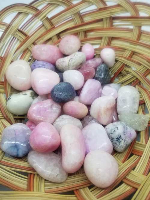 A woven basket filled with various smooth, colorful stones in shades of pink, purple, and white.