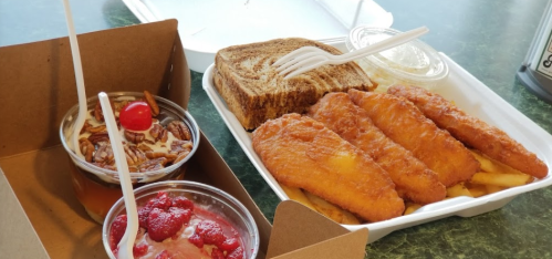 A takeout meal featuring fried fish fillets, fries, and two dessert cups with cherries and pecans.