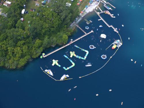 Aerial view of a lake with inflatable water attractions, docks, and people swimming and enjoying the water.