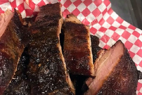 Sliced smoked brisket on a red and white checkered paper, showcasing a dark, caramelized crust.