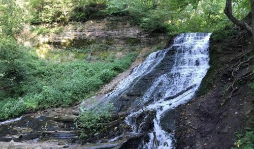 A serene waterfall cascading over rocky terrain, surrounded by lush green foliage and steep cliffs.