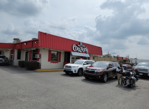 A red-roofed restaurant with a sign reading "Coo Jon's," surrounded by parked cars and a motorcycle.